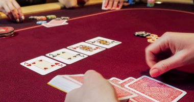 Kırmızı masada elinde fiş ve kartlarla poker oynayan kadın. Eline odaklan.