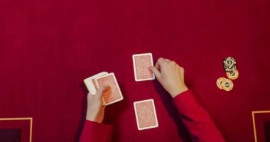 Kırmızı masada elinde fiş ve kartlarla poker oynayan kadın. Eline odaklan.
