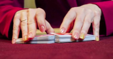 Kırmızı masada elinde fiş ve kartlarla poker oynayan kadın. Eline odaklan.