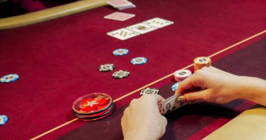 Kırmızı masada elinde fiş ve kartlarla poker oynayan kadın. Eline odaklan.