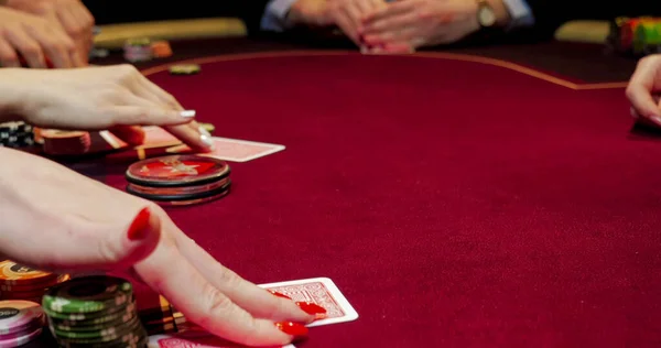 Woman playing poker in casino. Close up of female hands with red cards.