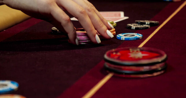Woman playing poker on red table with chips and cards. Focus on hand