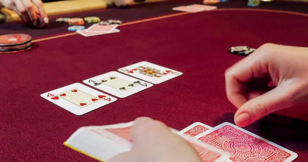 Kırmızı masada elinde fiş ve kartlarla poker oynayan kadın. Eline odaklan.