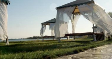 Sahilde, deniz kenarında bir çardak. Kumsal. Perdeler rüzgarda gelişir. Akşam ışığı Yazı