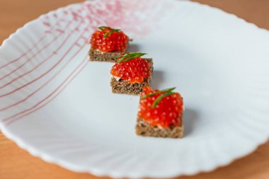 Ahşap bir masada kırmızı havyarla süslenmiş lezzetli sandviçler, güneş ışığıyla aydınlatılmış. Gurme yemek, lüks, şenlikli yemekler ve zarif mezeler için mükemmel bir tema.