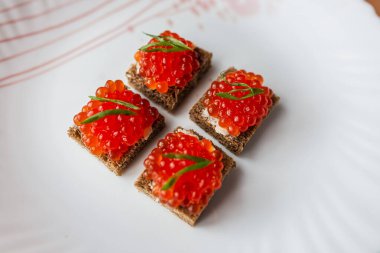 Ahşap bir masada kırmızı havyarla süslenmiş lezzetli sandviçler, güneş ışığıyla aydınlatılmış. Gurme yemek, lüks, şenlikli yemekler ve zarif mezeler için mükemmel bir tema.