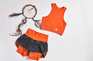 Pembe renkli atlet bluzu, şortu, uyumlu spor ayakkabısı ve beyaz arka planda metal bir taklacı da dahil olmak üzere şık bir spor kıyafetinin düz kompozisyonu. Fitness ve moda temaları için mükemmel