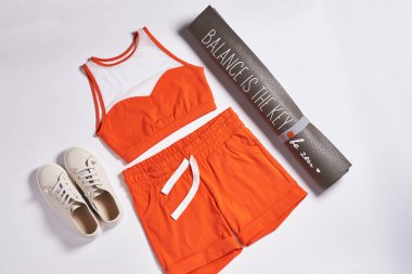 Pembe renkli atlet bluzu, şortu, uyumlu spor ayakkabısı ve beyaz arka planda metal bir taklacı da dahil olmak üzere şık bir spor kıyafetinin düz kompozisyonu. Fitness ve moda temaları için mükemmel