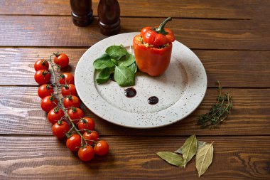 Doldurulmuş dolma dolma dolma biber, kiraz domatesleri ve ahşap bir masada otlardan oluşan canlı bir tabak..