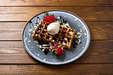 Üzerine bir top vanilyalı dondurma serpiştirilmiş, çikolata soslu ve taze çilek ve badem gevreğiyle süslenmiş lezzetli waffle 'lar.