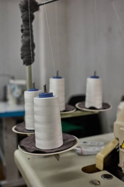 Endüstriyel dikiş makinesine birkaç beyaz iplik konisi yerleştirildi, bir giyim fabrikasında kullanıma hazır.