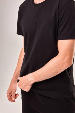 Bir adam tarafından giyilen siyah tişört, koluna, eline ve kumaş dokusuna vurgu yapıyor, gündelik moda sergiliyor, çok yönlü stil kavramı var.