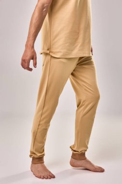 Bej renkli, rahat eşofmanlı, yalın ayaklı, erkek model, stüdyo ışıklarıyla yakalanmış, moda sadeliği kavramı.