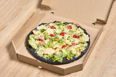 Üzerinde tavuk, marul, domates ve parmesan peyniri olan eşsiz bir siyah hamurlu pizza..