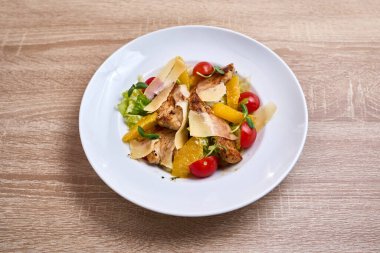 Grilled chicken salad with fresh oranges, cherry tomatoes, lettuce, and parmesan cheese shavings.