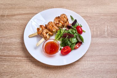 Izgara karides şişleri taze salata ve tatlı acı biber sosuyla servis edilir..