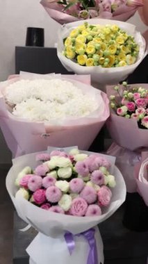 Pastel pembe kağıda sarılı çeşitli çiçek buketleri. Güller, kasımpatılar ve şakayıklar sergileniyor. Çiçek düzenleme konsepti.