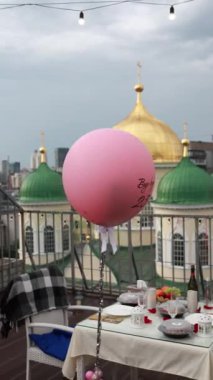 Pembe balon, şehir manzarası, şenlik masası kurulumu, görünür kubbeler, romantik akşam yemeği atmosfer ayarlama konsepti.