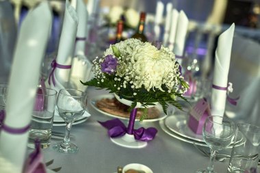 Çiçeklerle süslenmiş resmi yemek masası, mor kurdelelerle bağlanmış beyaz peçeteler ve zarif bir dekor için cam süsleme konsepti.