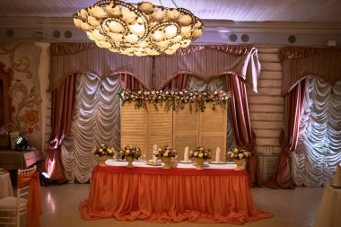 Düğün resepsiyon masası dekorunda zarif çiçek aranjmanları, mumlar ve sıcak ortam konseptinde lüks perdeler var.