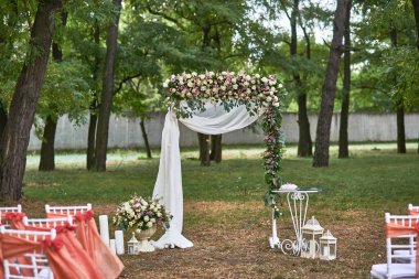 Çiçekler ve beyaz örtülerle süslenmiş düğün kemeri, doğal bahçe seremonisinde sandalyeler, büyüleyici titreşim, şenlikli sahne konsepti.