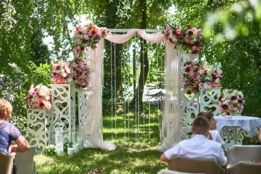 Sersemletici bir açık hava düğün sahnesi. Detaylı çiçek dekoru ve süslü kemer desenli yeşil çevre içinde, düğün düzenleme konsepti.