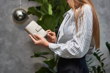 Çizgili gömlekli sofistike bir kadın, şık deri çantalı, iç mekan bitkileriyle donatılmış, şık bir moda anlayışı var.