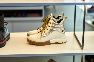 Metalik detayları ve sarı bağcıkları olan beyaz kış botları mağaza raflarında şık bir şekilde sergileniyor.