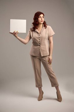 Ciddi bir ifadeyle, bej takım elbiseli kendine güvenen bir kadın boş kare tahta tutuyor, minimalist tarzda bir konsept.