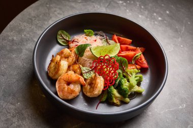 Sebzeli gurme karides salatası taze limon ve siyah tabakta servis edilen otlarla süslenmiş Asya mutfağı konsepti.