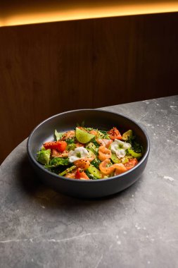 Avokado, domates ve somon salatası mermer yüzeyde siyah tabakta limonla süslenmiş, sağlıklı beslenme konsepti.