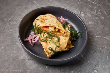 Peynirli, otlu ve soğanlı lezzetli bir quesadilla 'nın yakın plan görüntüsü taştan yapılmış koyu bir tabakta sunuluyor, Meksika yemeği kavramı.