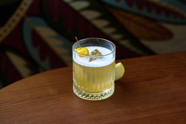 Kremalı köpükle kaplanmış ve bir kiraz ve bir dilim elmayla süslenmiş ferahlatıcı bir elma kokteyli. İçki renkli, desenli bir arka plana göre ayarlanır, davetkar ve şenlikli görünümüne eklenir..