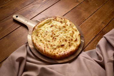 Eritilmiş peynir soslu taze Gürcistan khachapuri 'si, ahşap bir ahşap masa üzerinde bez ile servis edilir..