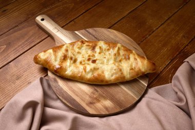 Erimiş peynirle dolu Gürcistan 'ın altın rengi khachapuri' si ahşap bir masanın üzerinde bez parçasıyla servis ediliyor..