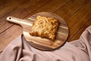 Tahta bir masanın üzerinde, ahşap bir kürek üzerinde servis edilen, altın-kahverengi kabuklu gevrek ve pullu kare puf böreği..