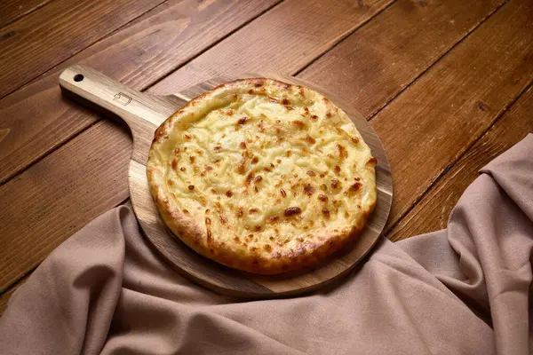 Eritilmiş peynir soslu taze Gürcistan khachapuri 'si, ahşap bir ahşap masa üzerinde bez ile servis edilir..