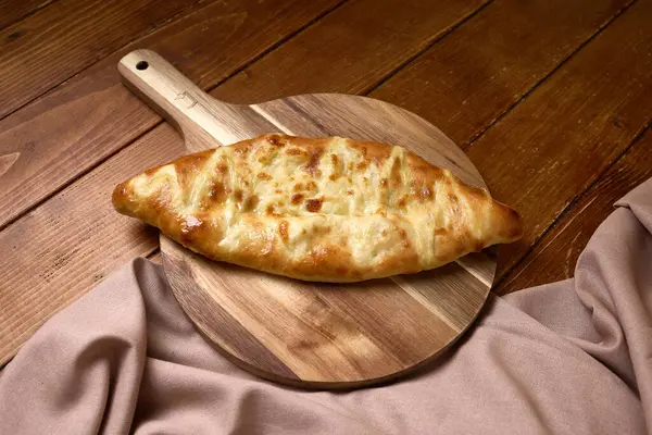 Erimiş peynirle dolu Gürcistan 'ın altın rengi khachapuri' si ahşap bir masanın üzerinde bez parçasıyla servis ediliyor..