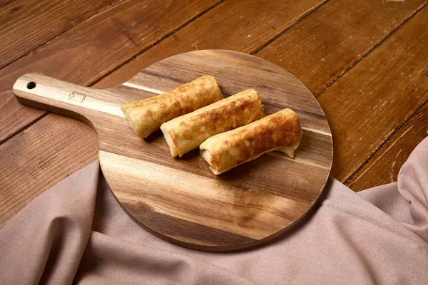 Üç gevrek, altın sarısı kızarmış börek, ahşap bir tahta kesme tahtasına yerleştirilmiş, sıcak ahşap bir masa arkasına kurulmuş..