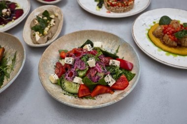 Feta peynirli canlı bir Yunan salatası, vişneli domates, salatalık, kırmızı soğan ve siyah susam tohumlarıyla süslenmiş taze yeşillikler..
