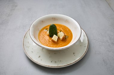 Bir kase kremalı havuç çorbası çıtır çıtır çıtır çıtır ve taze ıspanak yaprağı ile süslenmiş, zarif bir seramik tabakta servis edilir..