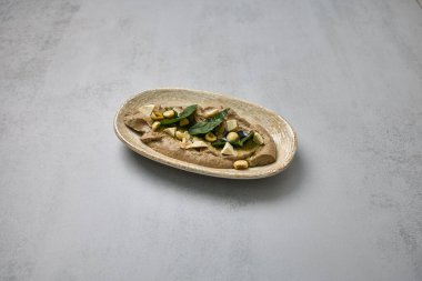 Tofu küpleri, fındıklar, taze ıspanak ve zeytin yağıyla süslenmiş, kırsal bir kasede servis edilen kremalı mantar humus yemeği..