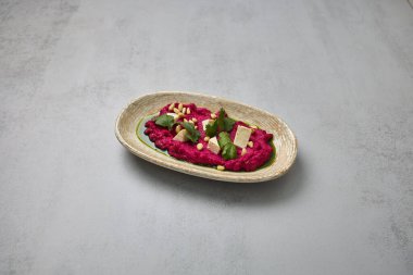 Taze kişniş, çam fıstığı ve yeşil yağlı tofu küpleriyle süslenmiş canlı pancar kökü humusu kırsal bir tabakta servis edilir..