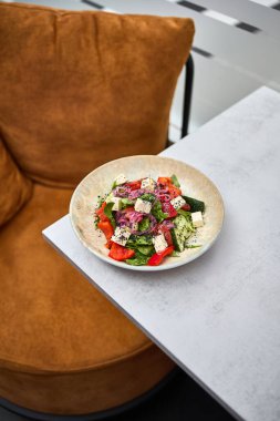 Feta peynirli, domatesli, salatalıklı ve soğanlı lezzetli bir Yunan salatası modern bir masada servis edilir..