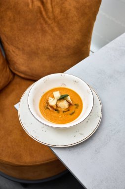 Sıcak bir kase kremalı balkabağı çorbası çıtır çıtır kıtır ekmek ve taze otlarla süslenmiş sıcak bir tabakta servis edilir..