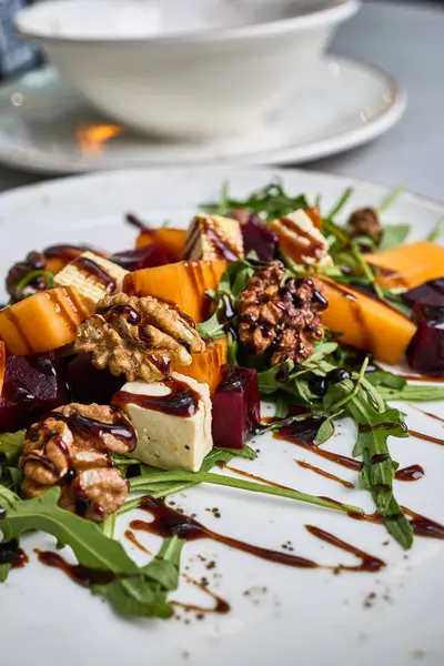 Beyaz bir tabakta kızarmış pancar, hurma, ceviz, roka, brie peyniri ve balzamik jöleli gurme salatasının detaylı bir görüntüsü..