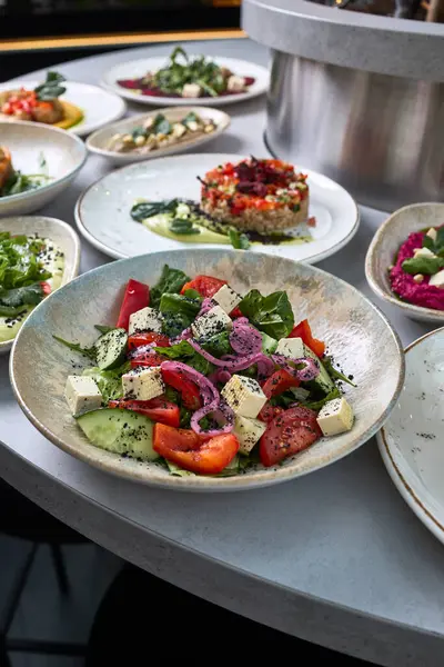 Feta peyniri, domates, salatalık, kırmızı soğan ve siyah susam tohumlu canlı bir Yunan salatası bir restoranda seramik kasede servis edilir..