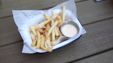 Üzerinde rendelenmiş parmesan peyniri ve ahşap bir masada kremalı sosla servis edilen kızarmış patates kızartması..
