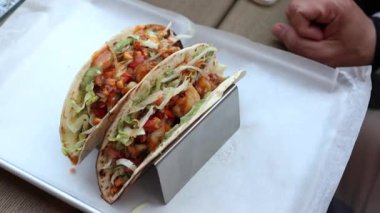 Metal tako tutacağında sebze, sos ve baharatla dolu iki karidesli taco, gündelik yemek için parşömen kaplı tepside servis ediliyor..