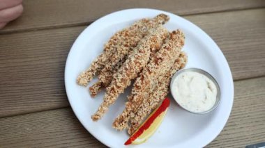 Beyaz bir tabakta, kremalı tartar sosu ve limon dilimi ile servis edilen altın ekmekli balık çubukları, günlük yemek için mükemmel..